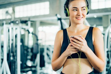 Kadın cep telefonu kullanıyor ve spor salonunda müzik dinliyor. Sağlıklı konsept, güzel spor kızı spor salonunda çalıştıktan sonra rahatlıyor..