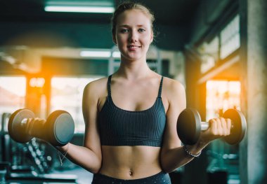 Spor salonunda spor yapmak için haltercilik oynayan genç bir kız, spor salonunda ağır halterleri kaldırıyor. Spor konsepti yağ yakma ve sağlıklı bir yaşam tarzı.