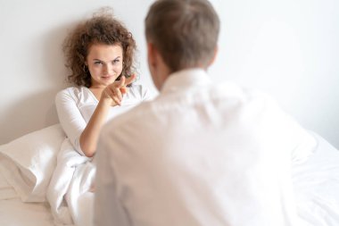 Young cute couple having fun together in bed, funny woman gesturing.