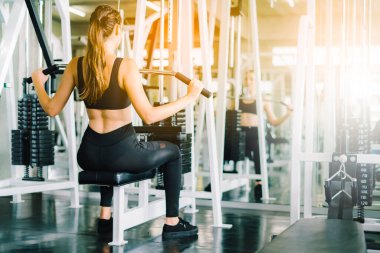 Genç fitness kızı spor salonundaki simülatörde asansörleri kaldırıyor. Spor salonundaki spor aletleriyle çalışan insanlar..