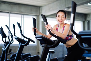 Young Asian woman exercising on bicycle in fitness center.