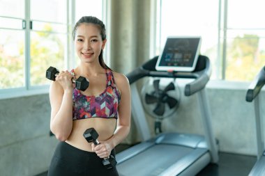 Young Asian girl using dumbbells to exercise in fitness club.