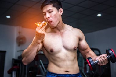 Strong muscular male athlete eating pizza fast food while training, unhealthy diet concept.