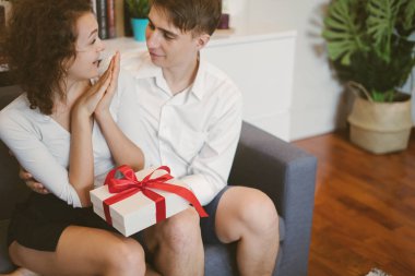 Young man surprising girlfriend with holiday present, boyfriend embracing lovely woman