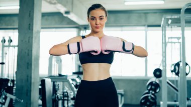 Boks eldivenlerinde poz veren kendine güvenen genç bir sporcunun portresi. Boks eldivenli bir çuvalı yumruklayan bir kadın..