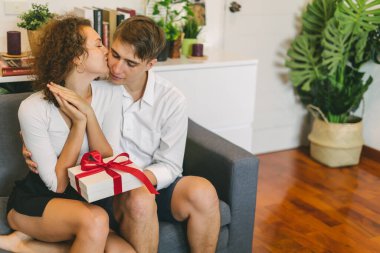 Young man surprising girlfriend with holiday present, woman kissing boyfriend at Valentines day