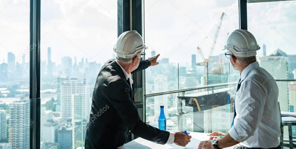 Two Engineer or Architect are analyzing blueprints while working on a new project on construction site with blue sky and city background.Architect supervising construction on terrace tower.