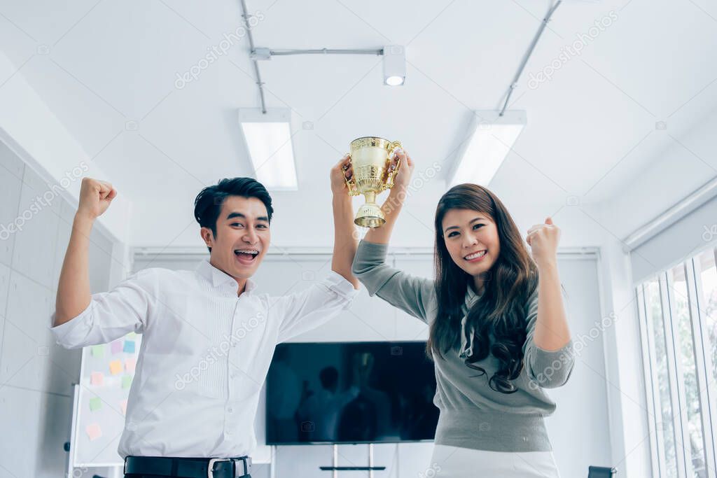 Businessman and Businesswomen team holding award trophy for show their victory.We are the champions! Successful business team with raised up hands in sunny modern workstation.