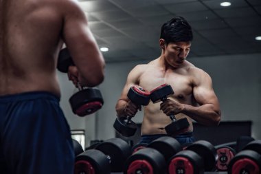 Man holding dumbbells in front of mirror in gym.