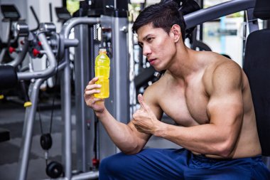 Asian man in gym holding electrolyte drink.