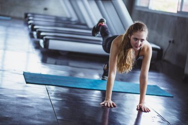 Spor salonundaki kadın esneme egzersizleri yapıyor ve zeminde gülümsüyor..