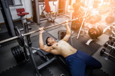 Muscular man in gym doing exercise with barbell, strong male.