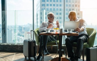 İki iş adamı pencerenin kenarında otururken el sıkışıyor. Olgun iş adamı, şehre tepeden bakan bir ofis kulesinde, modern bir iş yerindeki bir meslektaşıyla bilgi tartışıyor..