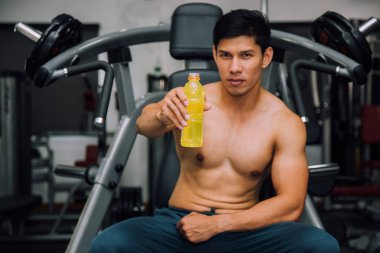 Asian fit man holding energy drink, relaxing and looking in camera in gym, sport and fitness concept.