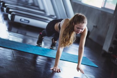 Spor salonundaki kadın esneme egzersizleri yapıyor ve zeminde gülümsüyor..