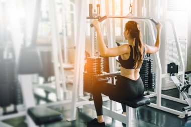 Genç fitness kızı spor salonundaki simülatörde asansörleri kaldırıyor. Spor salonundaki spor aletleriyle çalışan insanlar..