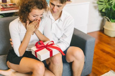 Young man surprising girlfriend with holiday present, boyfriend embracing pleased woman