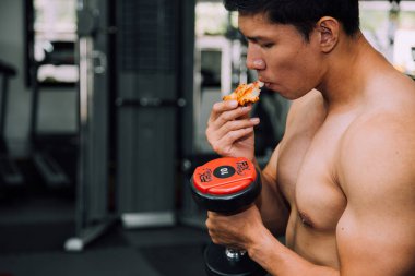 Strong muscular male athlete eating pizza fast food while training, unhealthy diet concept.