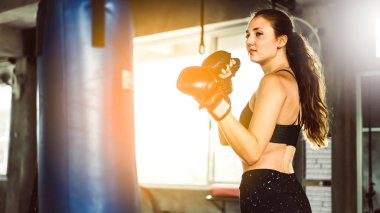 Spor salonunda kum torbasına yumruk atan genç bir kadın. Kickboks yapan kadın spor salonunda kum torbası yumrukluyor. Eğitimdeki kadın boksör..