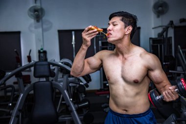 Strong muscular athletic man eating pizza fast food in gym, unhealthy eating diet concept.