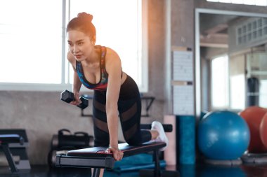 Young athletic woman working out with dumbbells in fitness club