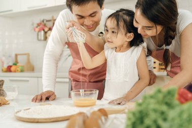 Evde sağlıklı yemekler ve mutfak konseptinde mutlu bir aile. Anne ve çocuk kahvaltı yapıyorlar. Sevimli küçük kız ve güzel anne ve babası mutfakta yemek yaparken kahvaltı hazırlıyorlar..