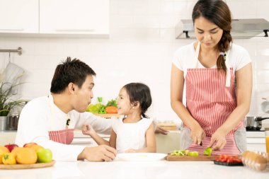 Evde sağlıklı yemekler ve mutfak konseptinde mutlu bir aile. Anne ve çocuk kahvaltı yapıyorlar. Sevimli küçük kız ve güzel anne ve babası mutfakta yemek yaparken kahvaltı hazırlıyorlar..