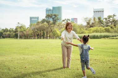 Güzel küçük kız parkta büyükannesinin kucağına koşuyor. Büyükannesi ve torunu güneşli bahçe tatilinin tadını çıkarıyorlar. Açık havada, boş bir yerde..