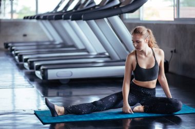 Spor salonundaki kadın esneme egzersizleri yapıyor ve zeminde gülümsüyor..