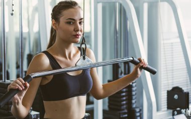 Genç fitness kızı spor salonundaki simülatörde asansörleri kapatın. İnsanlar spor salonundaki spor aletleriyle spor yapıyor..