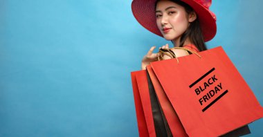 Pleased young Asian woman holding red shopping bags on blue background, copy space, Black Friday and shopping concept.