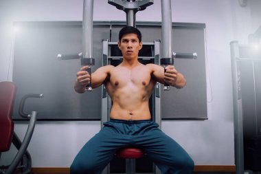 Athletic muscular bodybuilder training on machine in gym, strong male.