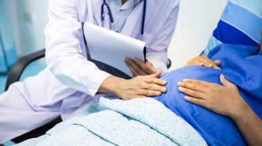 Doktor Holding 'in not defterine bakmasından hamile kadın ve erkek doktor Steteskoplu hamile kadın ve erkek doktor.