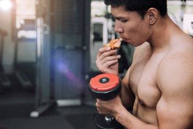 Strong muscular male athlete eating pizza fast food while training, unhealthy diet concept.