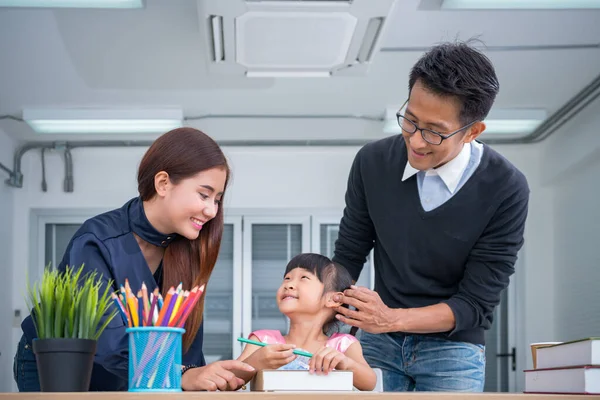 Güzel Asyalı kadınlar ve baba, kızına ev ödevlerinde yardım ediyor. Aile annesi, kızına evde okuma-öpme öğretiyor..