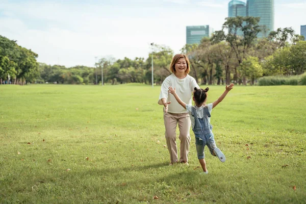 Nice little girl run to grandmother\'s hug in park.Grandmother and grand daughter enjoying sunny garden holiday together, outdoors space, leisure lifestyle,happy teaching with flare light sky in park.