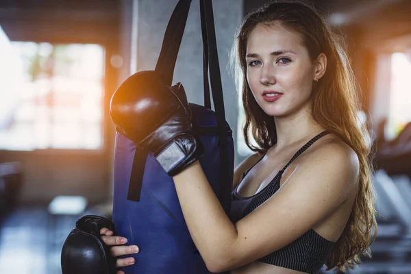 体育館で重い袋にパンチ若いスポーティ女性 体育館で袋を蹴るキックボクシングの女性 トレーニングで魅力的な女性ボクサー — ストック写真