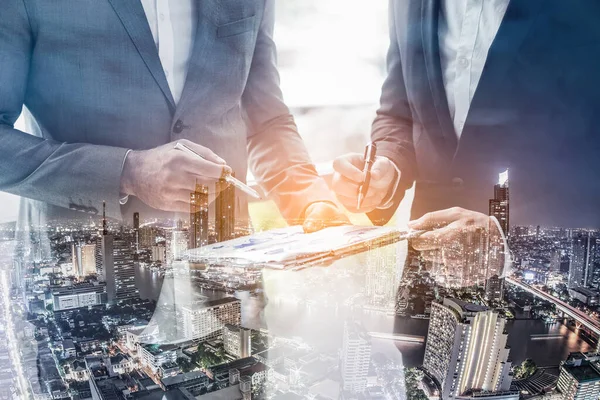 Double exposure of business signing for successful of investment deal and city night background, teamwork and partnership concept. Business man signing a contract.