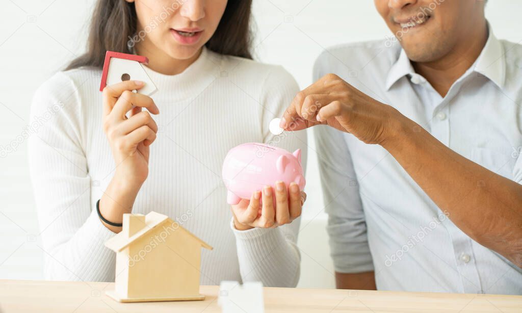 Man putting a coin into a pink piggy bank concept for savings and finance.The best choice of house.House owner and architect discussing a choice.Couple dreaming of new home.