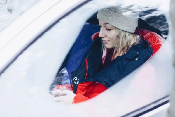 The girl in the winter clothes in the car looks at the phone — Stock Photo, Image