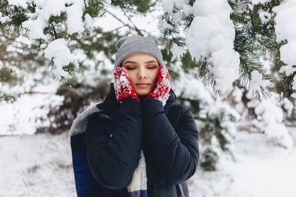 The girl warmes her cheeks in gloves at the cold winter in the p — Stock Photo, Image