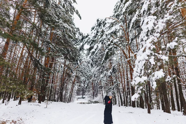 A menina caminha em uma floresta coberta de neve entre os pinheiros em g vermelho — Fotografia de Stock