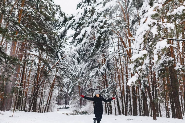 Het meisje loopt in een besneeuwd bos onder de dennen in rode g — Stockfoto