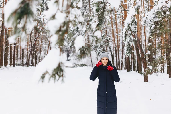 The girl walks in a snow-covered forest among the pines in red g — Stock Photo, Image