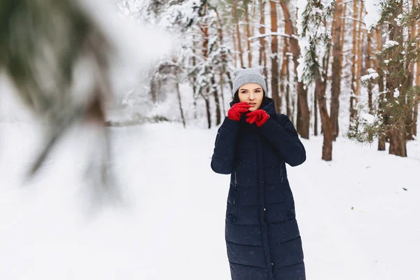 Dívka chodí v zasněženém lese mezi borovicemi v červené g — Stock fotografie