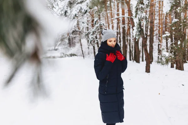 A menina caminha em uma floresta coberta de neve entre os pinheiros em g vermelho — Fotografia de Stock