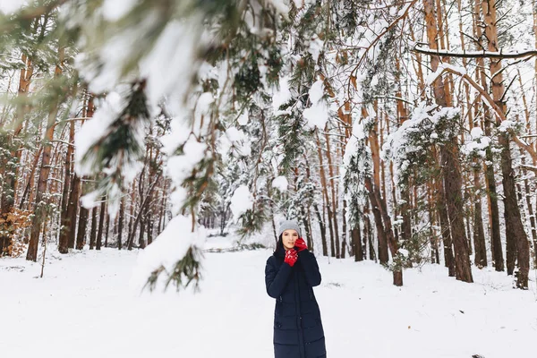 A menina caminha em uma floresta coberta de neve entre os pinheiros em g vermelho — Fotografia de Stock