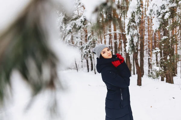 A menina caminha em uma floresta coberta de neve entre os pinheiros em g vermelho — Fotografia de Stock
