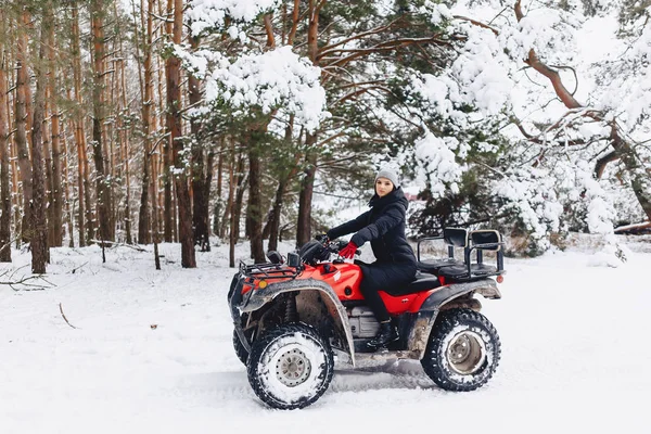 Jong meisje op een motorfiets rijdt in sneeuw bedekte dennenbos in — Stockfoto