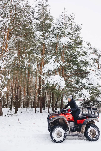 Jong meisje op een motorfiets rijdt in sneeuw bedekte dennenbos in — Stockfoto